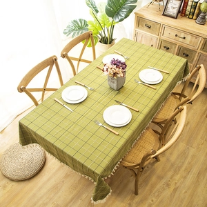 Detail of green plaid tablecloth with white fringe trim on a rectangular wooden table