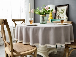 Close-up of a light grey round tablecloth featuring delicate white lace tassel edges