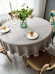 Close-up of a light grey round tablecloth featuring white lace tassels and linen texture