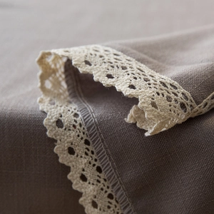 Detail of waterproof dark taupe linen tablecloth featuring white crochet lace trim edges