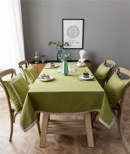 Detail of green linen tablecloth with floral lace border and matching cushions on wood table
