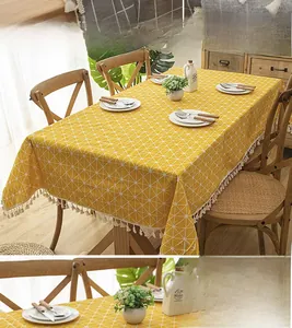 Detail of yellow checkered tablecloth with white tassels on a wooden dining table