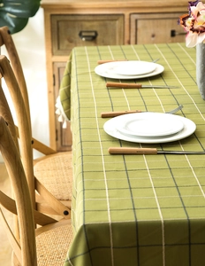 Detail view of green plaid tablecloth with white fringe tassels on a wooden table