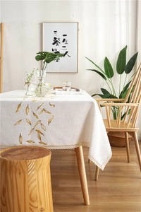 Close-up of cream rectangular tablecloth with yellow leaf embroidery and fine lace edge