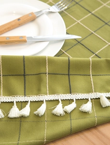 Detailed view of green plaid tablecloth with thick texture and elegant white tassel trim
