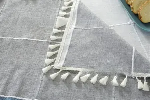 Detailed macro view of gray and white plaid fabric featuring delicate white cotton tassels