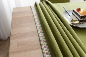Detail of green tablecloth fabric with floral embroidery on wooden dining table