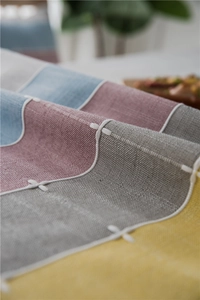 Detail of color-block linen table runner with white cross-stitch and tassel texture