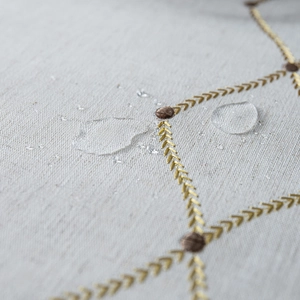 Macro detail of waterproof fabric with gold diamond embroidery and rolling water droplets