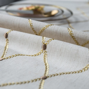 Detail view of golden wheat embroidery on light beige textured linen-style tablecloth