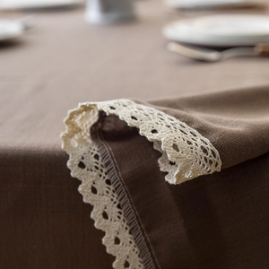 Detail of coffee brown linen tablecloth featuring white crochet lace edge and rustic texture
