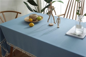 Detail of sky blue waterproof tablecloth with white tassel edges on a wooden table