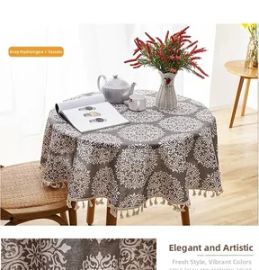 Detail of round grey linen-style tablecloth with white floral pattern and beige tassels