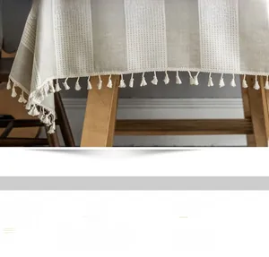 Detail of grey geometric linen tablecloth featuring hand-woven beige fringe tassels