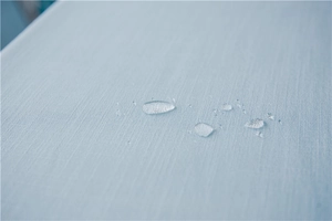 Macro shot of waterproof light blue faux linen fabric with clear water beads on surface