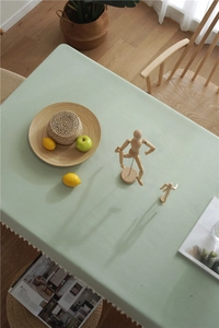 Detail of light green linen tablecloth with elegant white fringe edges on wooden table