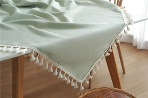 Close-up of mint green cotton linen tablecloth featuring decorative white fringe tassels