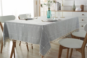Detail of grey checkered linen tablecloth with white cotton tassels on a wooden table