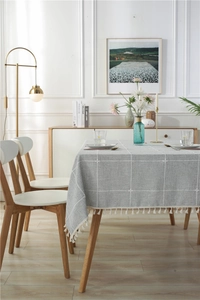 Detail shot of grey plaid tablecloth with elegant cream tassels on a wooden dining table