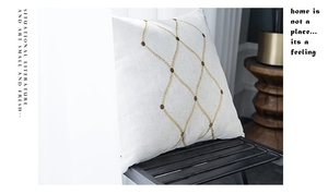 Detail of white cotton linen cushion with gold embroidered geometric patterns on a bench
