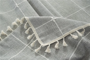Detailed close-up of grey plaid tablecloth featuring white embroidery and fringe trim