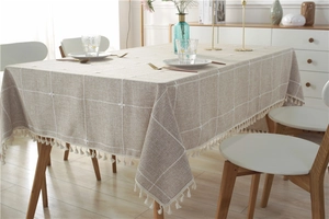 Detailed view of white floral embroidery and tassel fringe on beige linen tablecloth