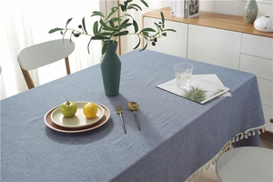 Detailed view of blue-grey textured tablecloth with white fringe and home decor