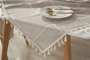 Close-up of khaki linen tablecloth with white floral embroidery and tassel fringe details
