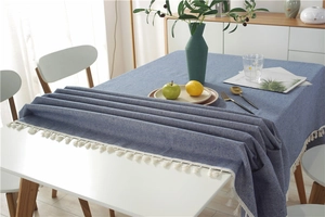 Detailed close-up of blue linen textured tablecloth with white tassel fringes in a home setting