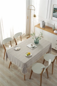 Close-up of light gray embroidered tablecloth with chic tassels on a wooden dining table