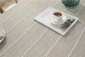 Close-up of linen-textured tablecloth featuring white geometric chain embroidery and tassels