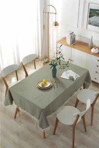 Detailed texture of grey-green linen-cotton tablecloth with white fringe on a wooden table