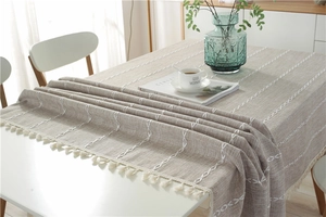 Detailed view of beige faux linen tablecloth with white embroidery stripes and fringe edge