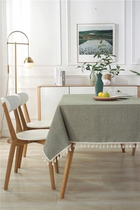 Close-up of sage green woven tablecloth featuring elegant white tassel fringe edges