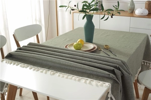 Close-up of sage green tablecloth with white cotton tassel fringe and woven texture