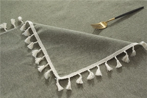 Close-up of minimalist green table cloth with cotton linen texture and fringe trim