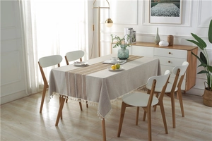 Close-up of beige linen tablecloth featuring brown striped patterns and white cotton tassels