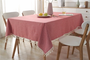 Detail of coral red woven tablecloth with white fringe tassels on a wooden dining table