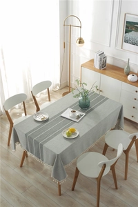 Detailed view of grey linen tablecloth with white lace patterns and decorative tassels