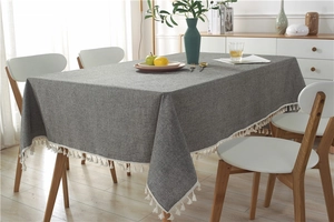 Detailed view of grey textured fabric with white fringe tassel edges on a wooden table