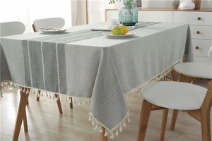 Detailed close-up of striped linen tablecloth featuring white pom-pom fringe and woven texture