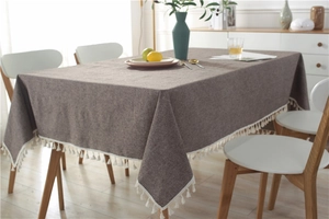 Detail of grey-brown woven tablecloth with elegant white fringe trim on a wooden table