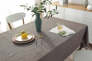 Close-up of grey textured cotton linen tablecloth with beige fringe tassels on a dining table