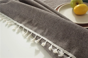 Detailed close-up of textured gray tablecloth with decorative white tassels and fruit
