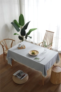 Close-up of light blue linen tablecloth with white tassel fringe on a wooden table
