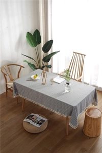 Detail of grey plaid tablecloth featuring white tassel edges on a wooden table surface