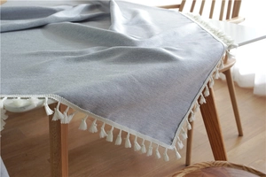 Detail of light blue-gray tablecloth with elegant white tassels and linen texture