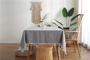 Close-up of grey plaid tablecloth with white pom-pom fringe on a wooden dining table