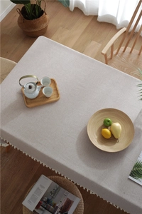 Detailed close-up of beige linen tablecloth fabric texture and white fringe tassels decoration