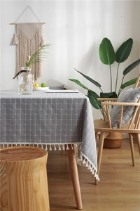 Detail of grey plaid tablecloth with white fringe tassels on a rustic wooden table